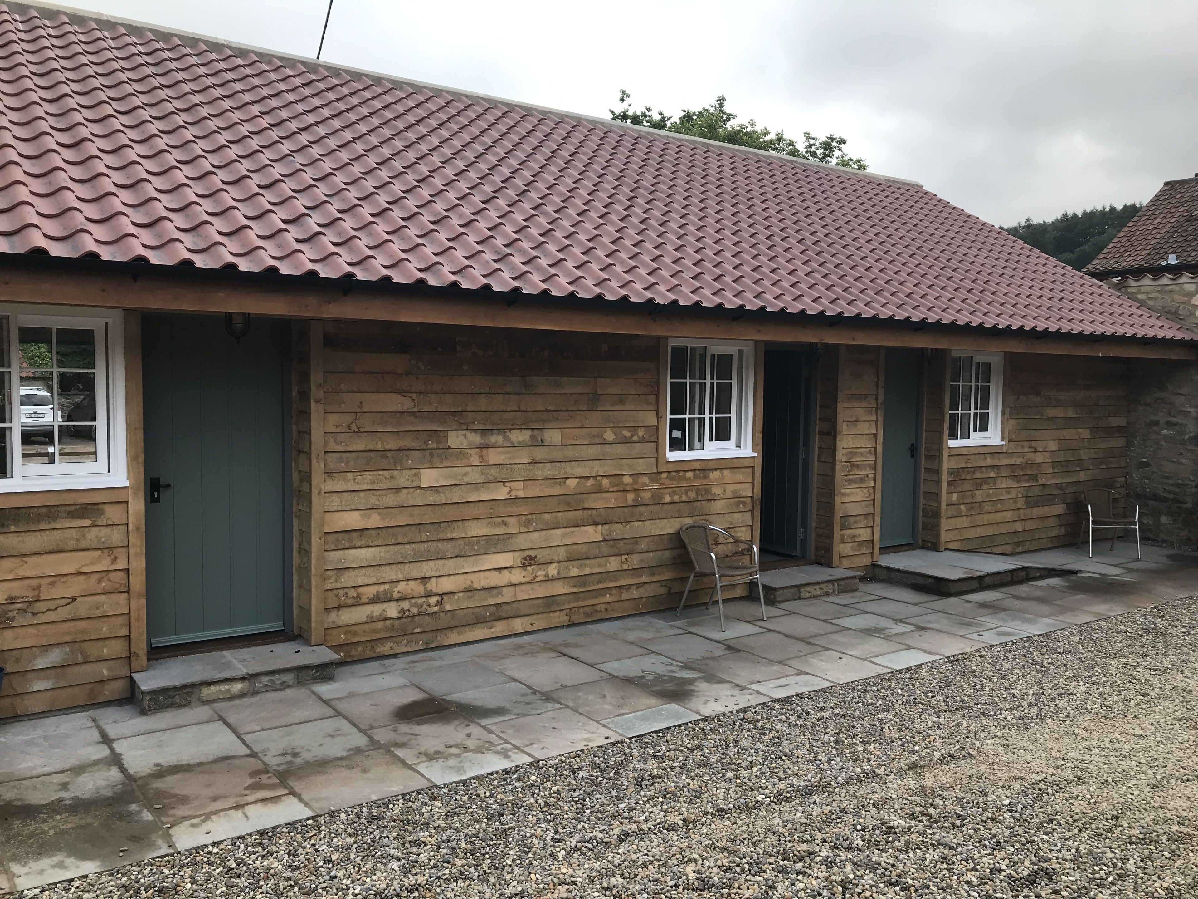 A wooden building with a tiled roof, a gravel driveway, and a small outdoor seating area.