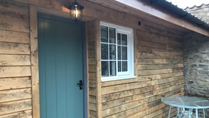 A wooden cabin with a teal door, a window, and a small patio table. - The Crown - Hutton le Hole (York)