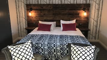 Un dormitorio con cabecera de madera, dos lámparas de noche, una colcha estampada y dos sillones con cojines decorados.
