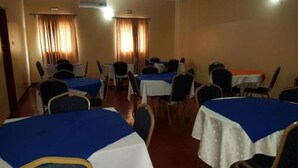 A hotel room with multiple tables and chairs, arranged in a conference room style. - Zuus Lodge & Tours (Kalomo)