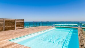 A pool area with a wooden deck, a glass railing, and a view of the ocean. - Horizon Breeze 1102 (Cape Town)