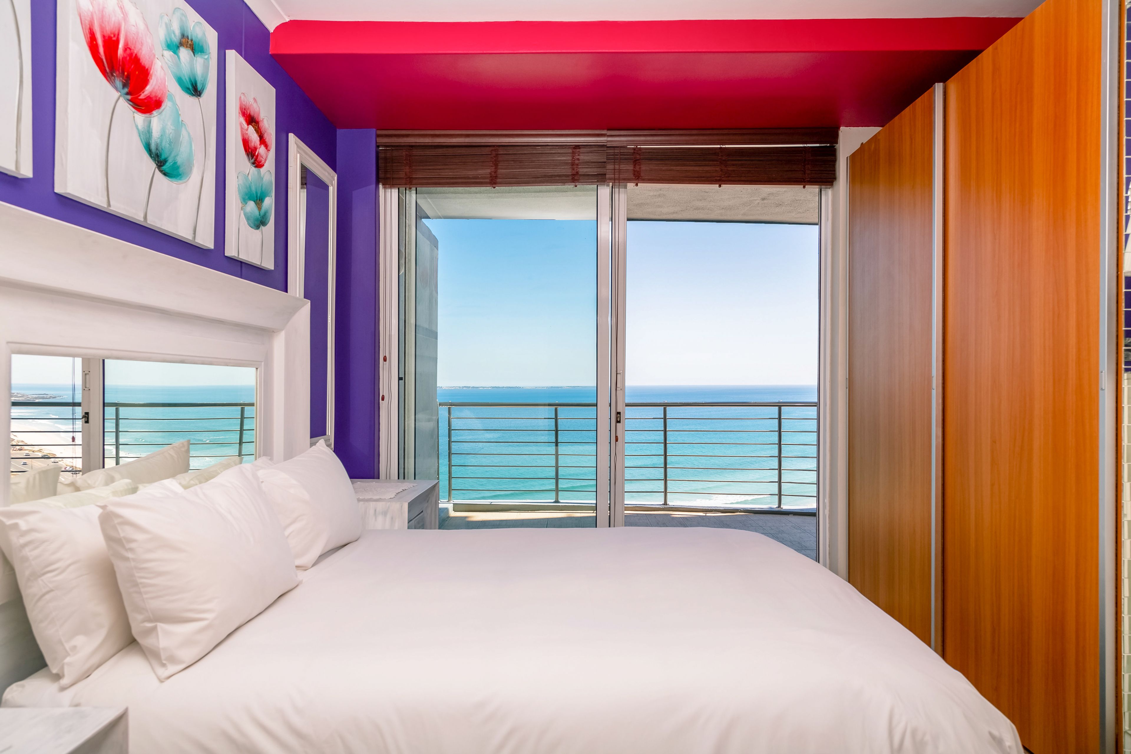 A bedroom with a large bed, a view of the ocean, and a balcony with a railing.