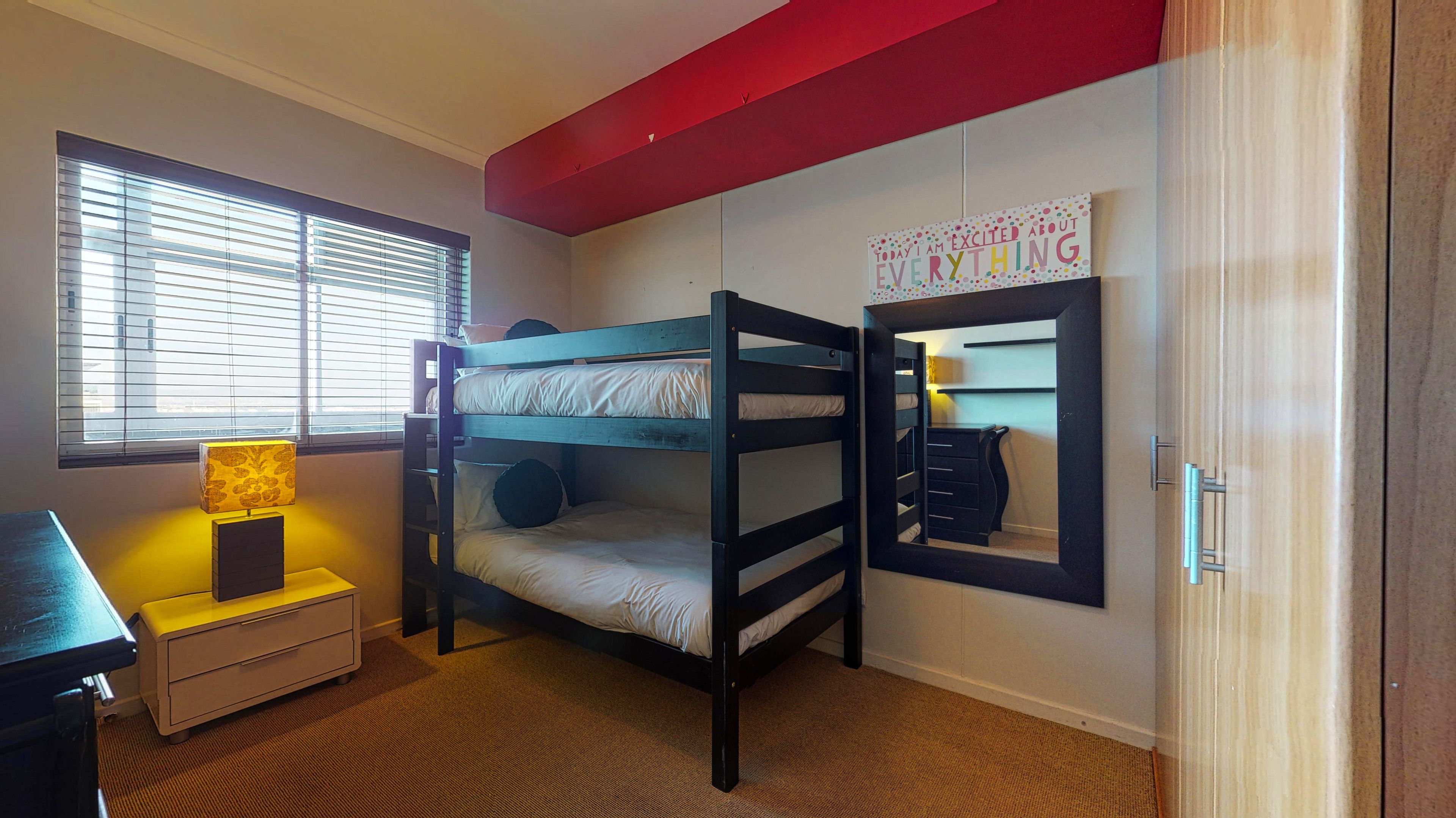 A bunk bed room with a desk, a lamp, and a motivational poster.