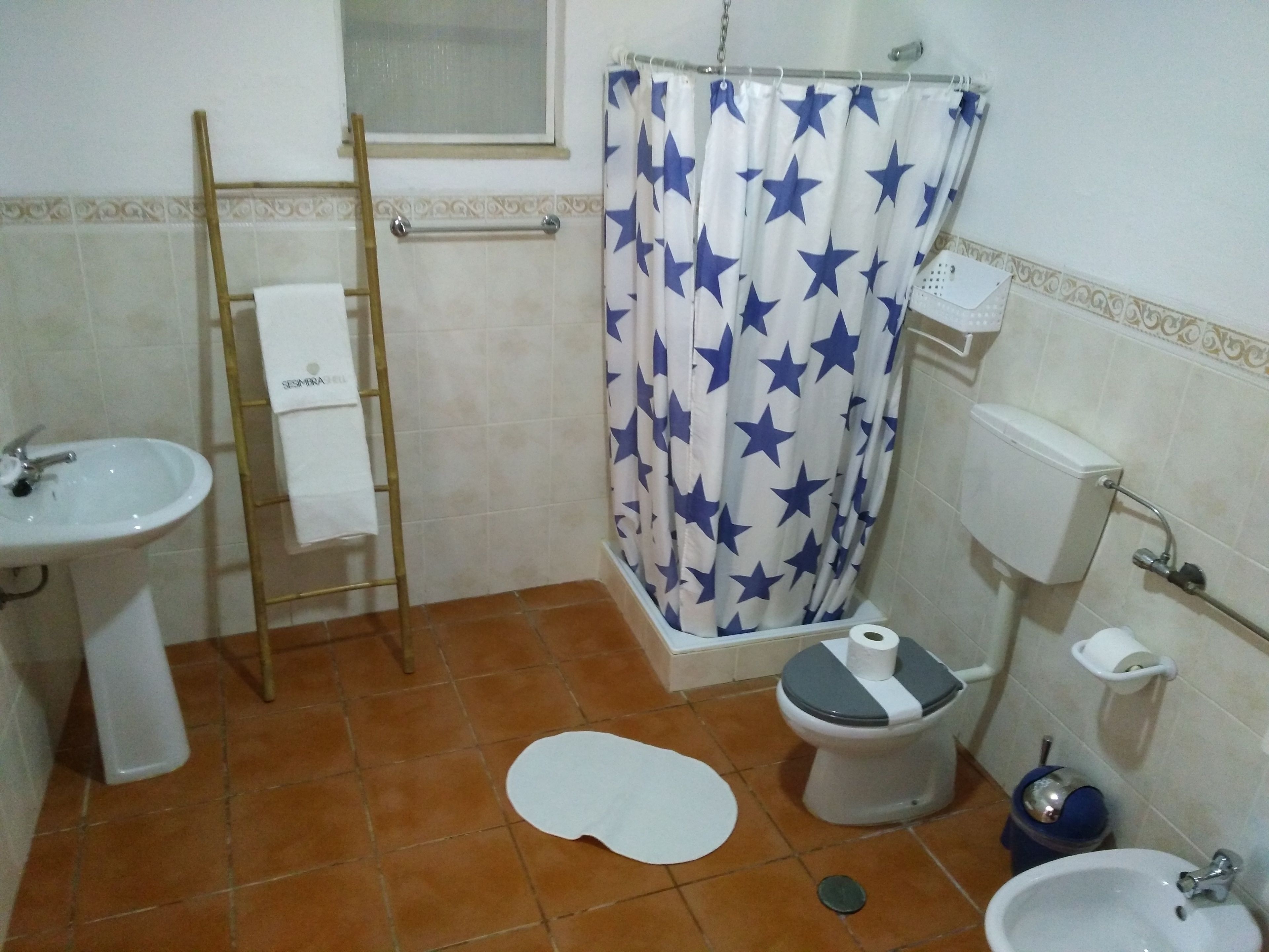 A bathroom with a shower curtain, toilet, bidet, sink, and a towel rack.