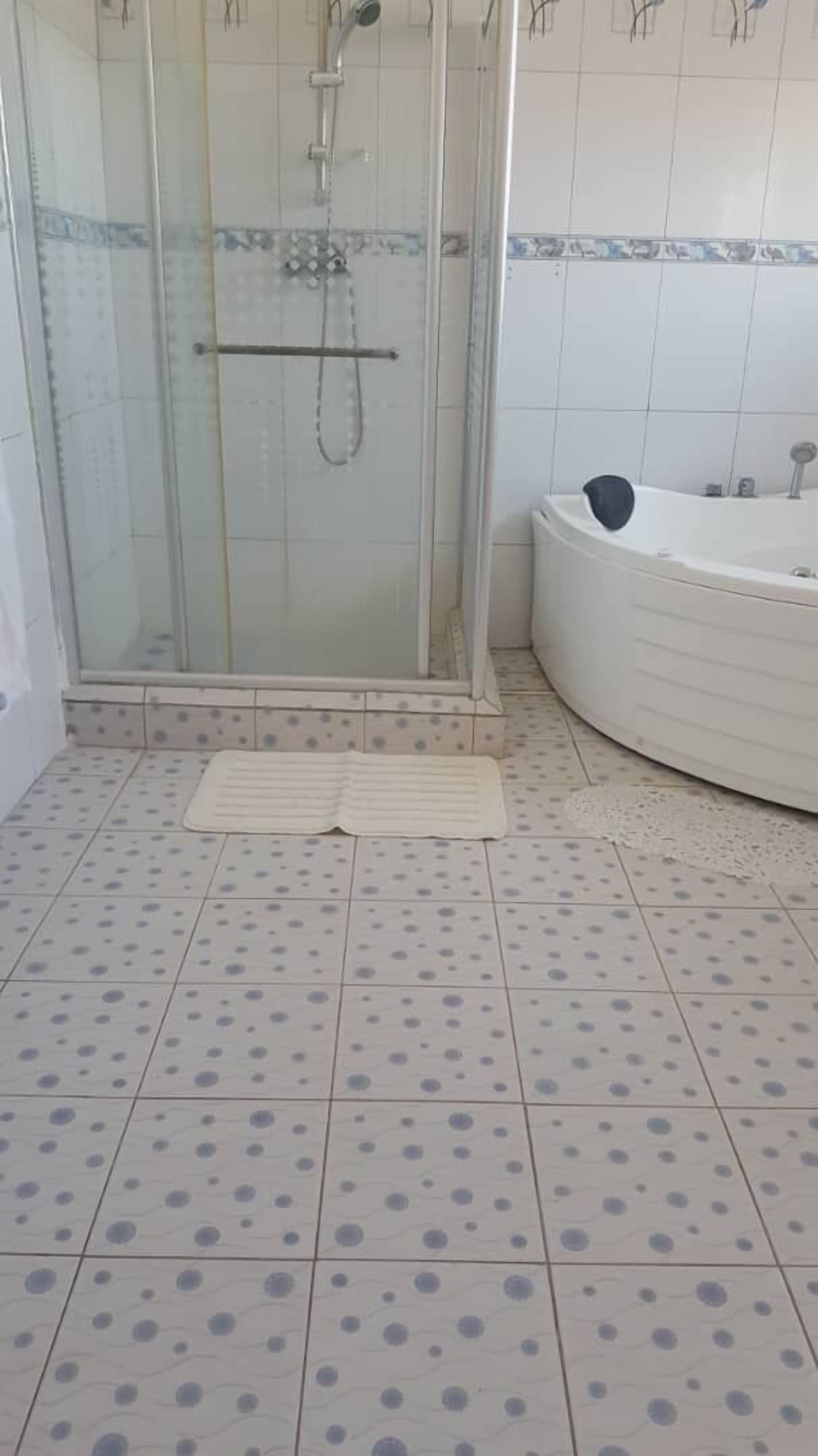 A bathroom with a glass-enclosed shower, a white bathtub, and a tiled floor with a polka dot pattern.