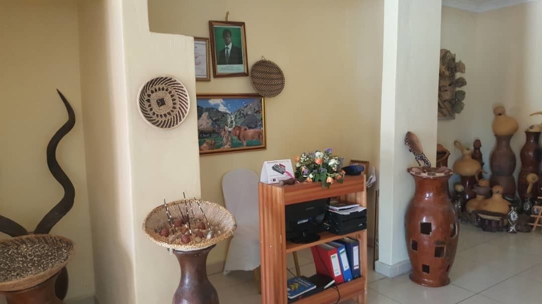 A room with a wooden bookshelf, a framed picture, a decorative basket, and a collection of pottery on the right side.