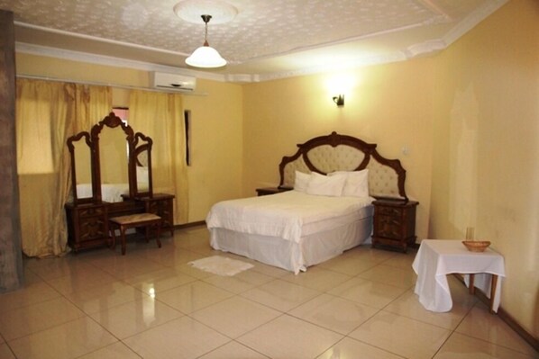 A hotel room with a bed, a vanity with a mirror, a small table with a candle, and a ceiling fan.