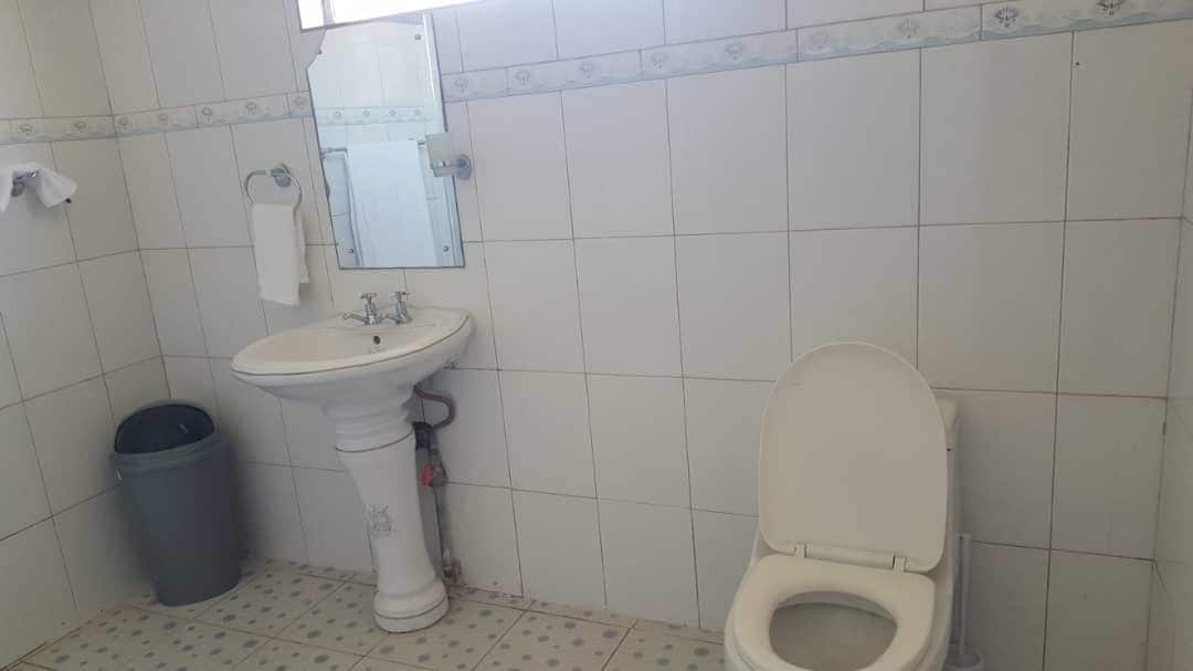 A small bathroom with a white sink, a toilet, and a trash can.
