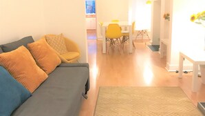 A living room with a grey sofa, yellow chairs, a white table, and a patterned rug. - Seaside House With Parking (Worthing)