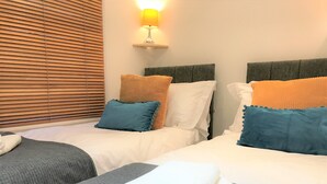 A hotel room with two beds, each with white bedding and orange and blue pillows. There is a lamp on a bedside table, and a folded white towel on the bed. - Seaside House With Parking (Worthing)