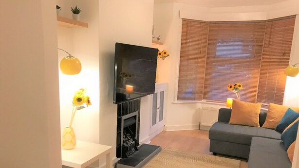 A living room with a flat-screen TV mounted above a fireplace, a sofa with cushions, a small table, and a rug. - Seaside House With Parking (Worthing)