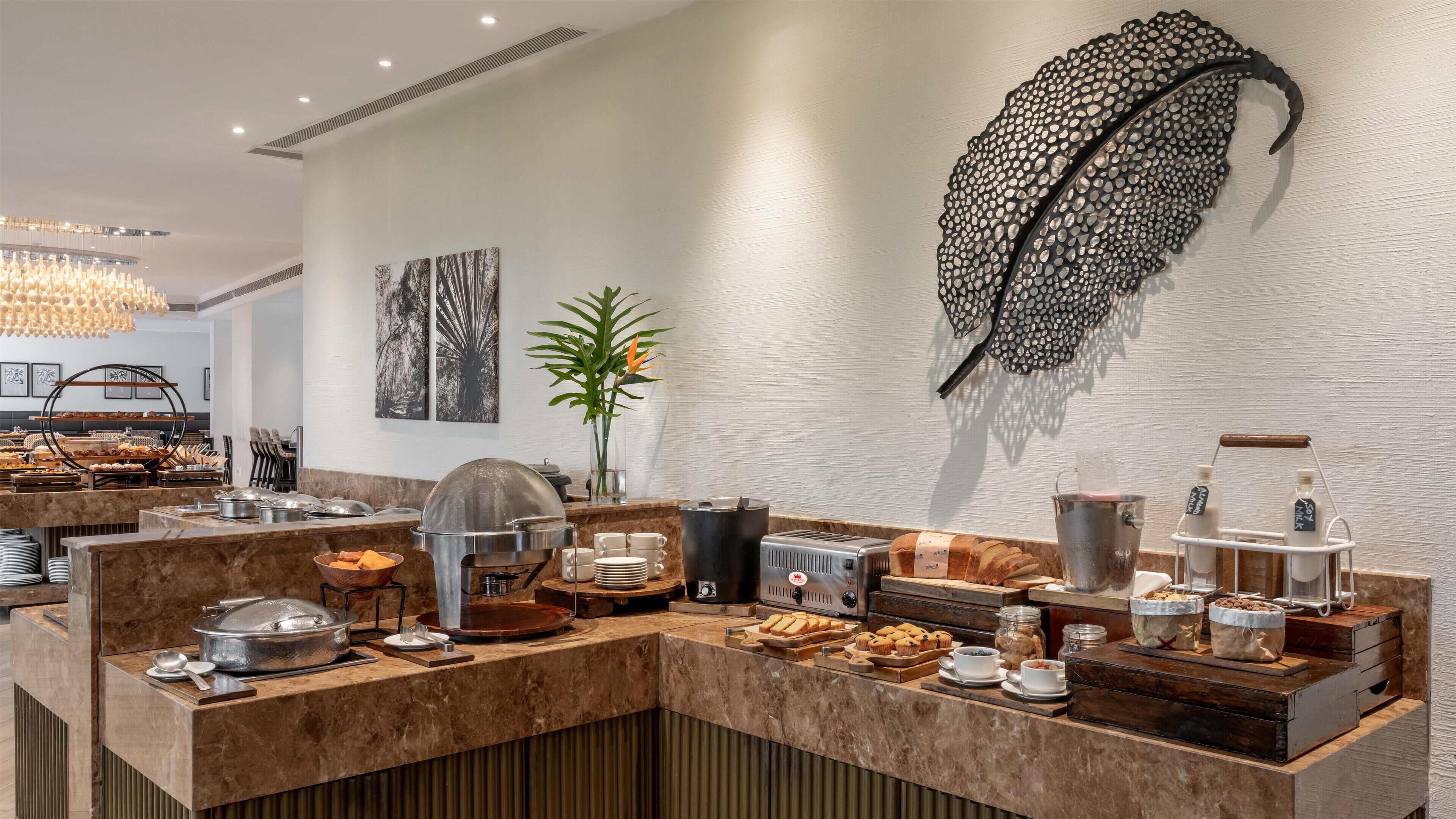 A modern breakfast buffet with a variety of food items, a coffee station, and a decorative feather wall piece.