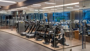 Een moderne sportschool met diverse fitnessapparaten, glazen wanden en een houten vloer.