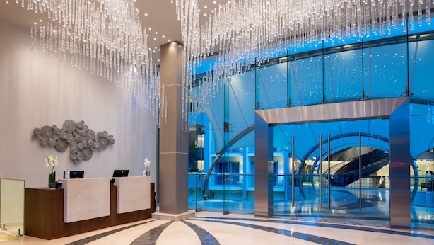 Een ruime lobby met een receptiebalie, een grote glazen wand en een unieke lichtinstallatie.