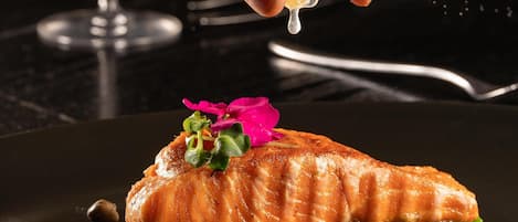 A hand squeezing a lemon over a plate of food.
