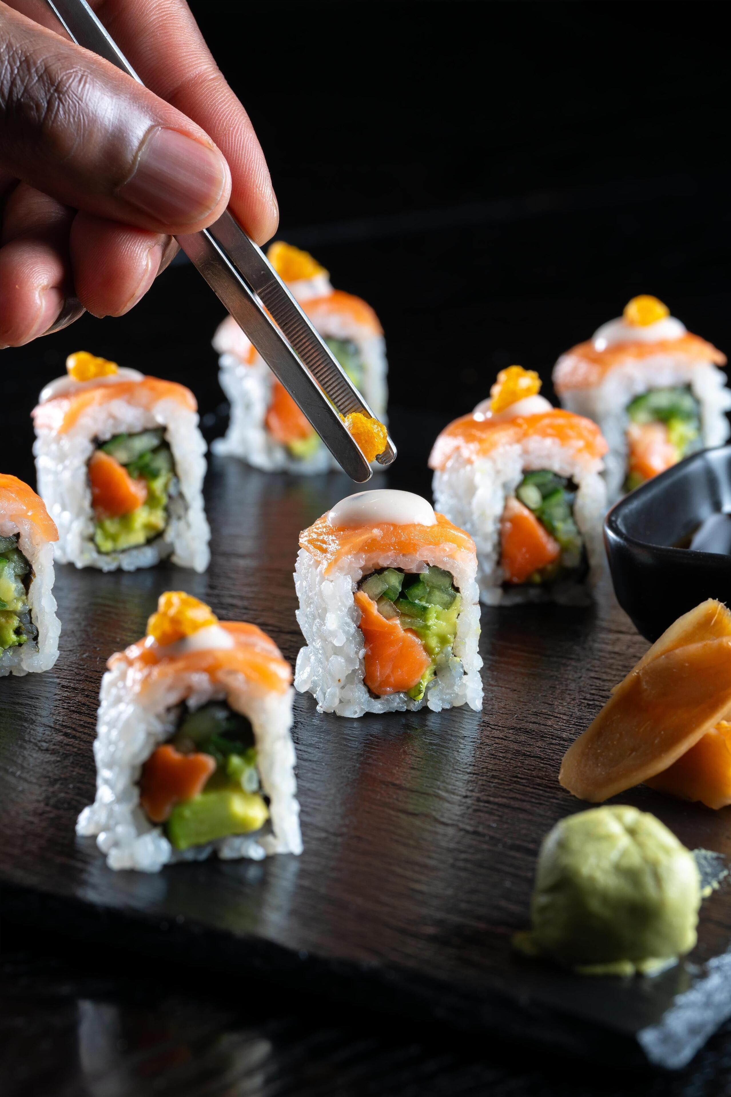 A sushi platter with various pieces, including salmon and avocado, on a dark wooden table.