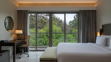 A hotel room with a large bed, a desk with a chair, a small table, and a large window with curtains.