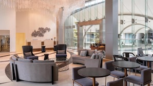 Een ruime lobby met modern meubilair, een grote kroonluchter en een glazen wand met uitzicht op het interieur.