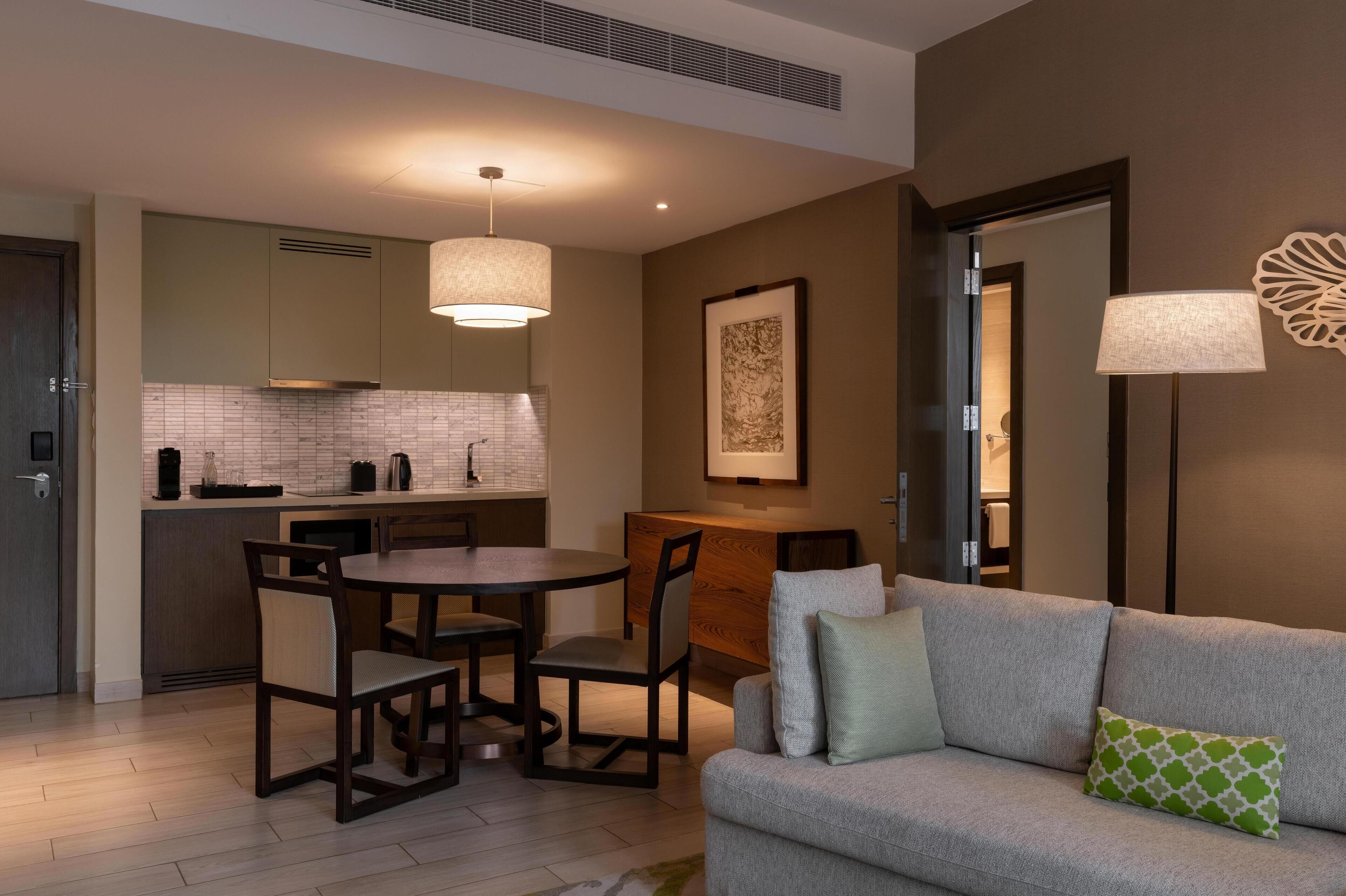 A modern hotel room with a dining area, a sofa, and a lamp.
