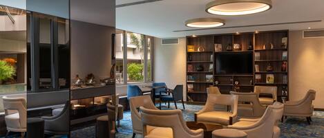 A modern lounge area with leather chairs, a bookshelf, and a flat-screen TV.
