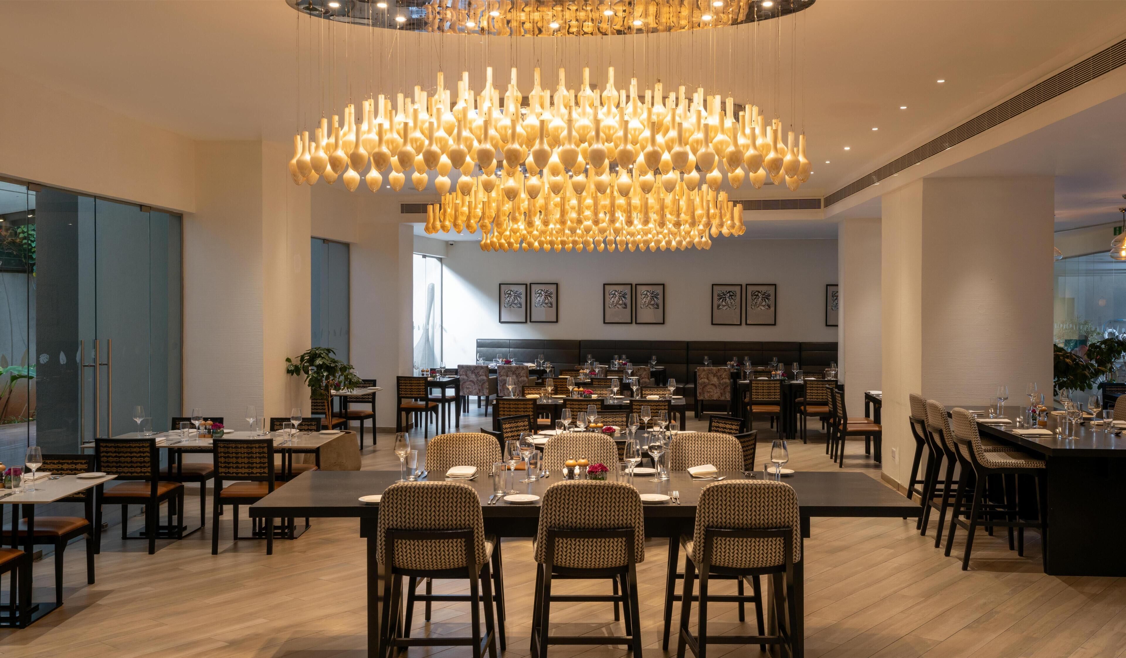 A modern dining area with a large chandelier, multiple dining tables, and chairs.