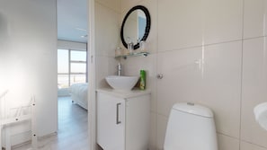 A modern bathroom with a white sink, a glass bowl, a green bottle, and a toilet. - The Bay Views (Cape Town)