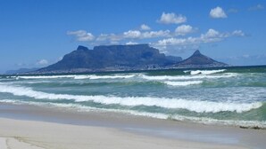 A beach with waves, a mountain in the background, and a clear sky. - The Bay Views (Cape Town)