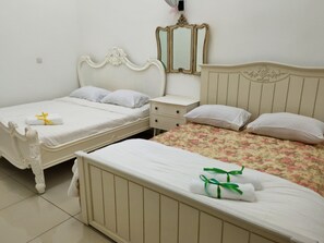 Classic hotel room with two single beds and a larger bed, each with its own pillow and bedside table.