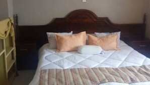 A neatly made bed with a patterned bedspread and two pillows, a wooden headboard, and a mosquito net hanging above. - Twana Classic Lodge (Choma)