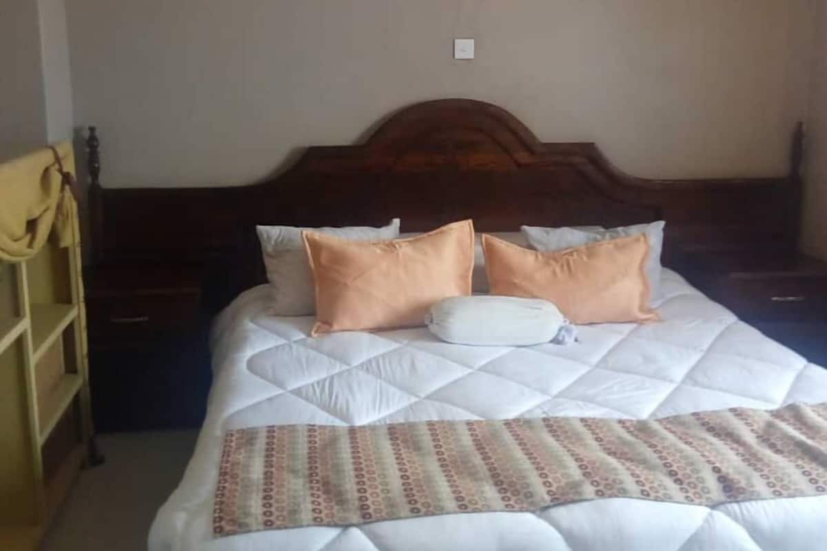 A neatly made bed with a patterned bedspread and two pillows, a wooden headboard, and a mosquito net hanging above.