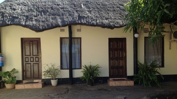 A building with a thatched roof, two wooden doors, and potted plants in front. - Twana Classic Lodge (Choma)