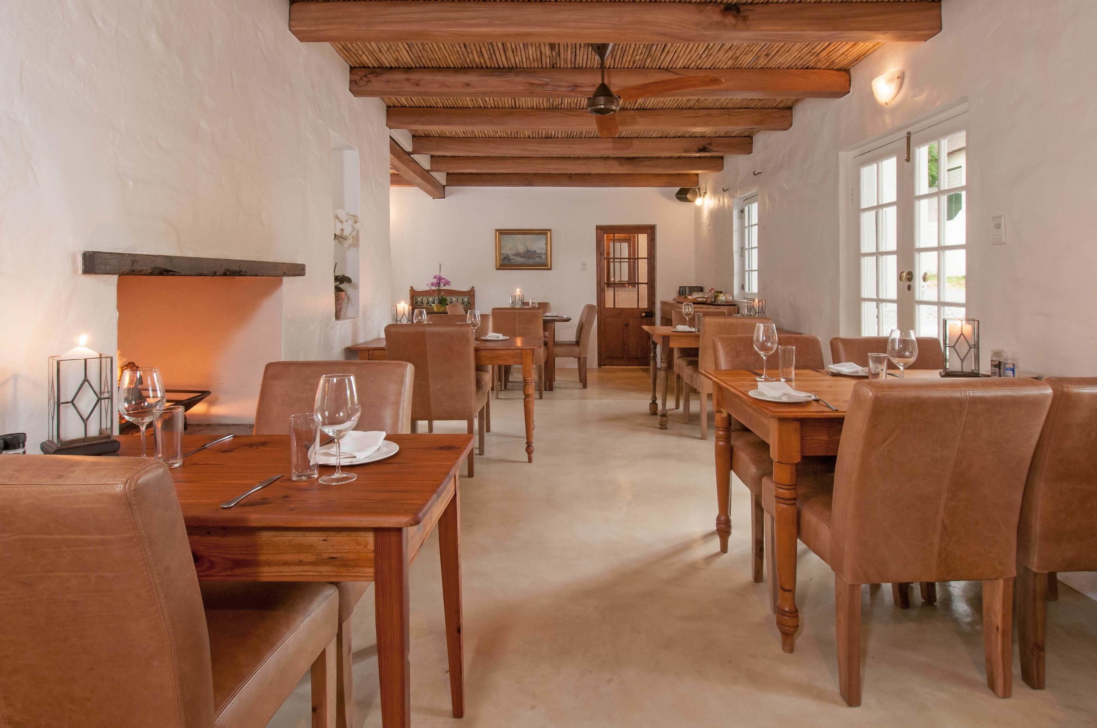 A dining area with wooden tables and chairs, a ceiling fan, and a painting on the wall.