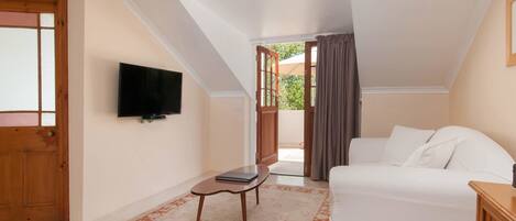 A bedroom with a bed, a television mounted on the wall, a small table, and a door leading to an outdoor area.