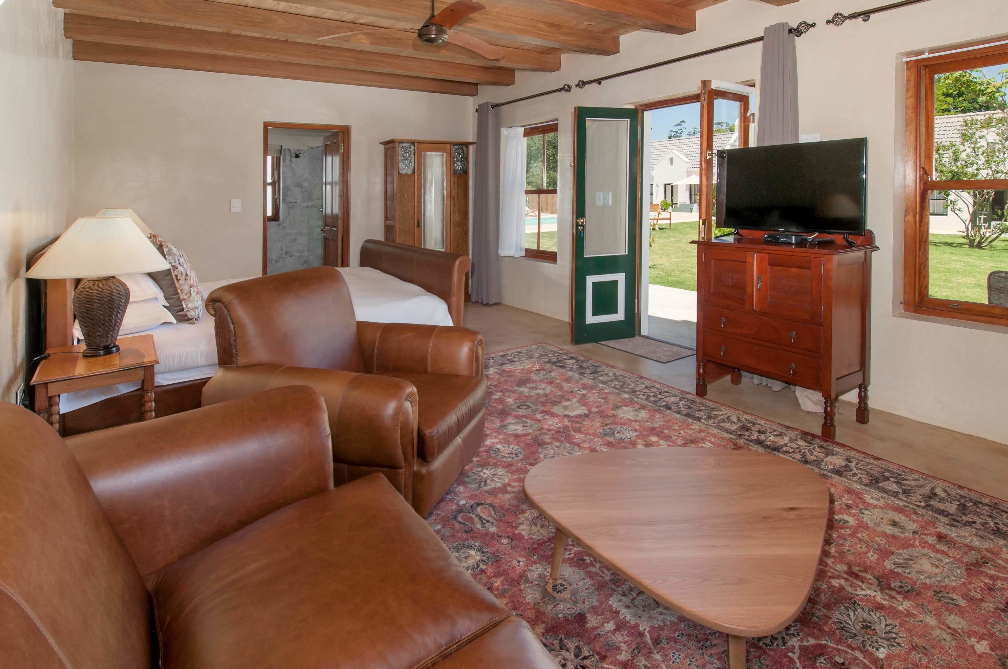 A room with a bed, leather sofa, a wooden coffee table, a TV on a wooden cabinet, and a patterned rug.