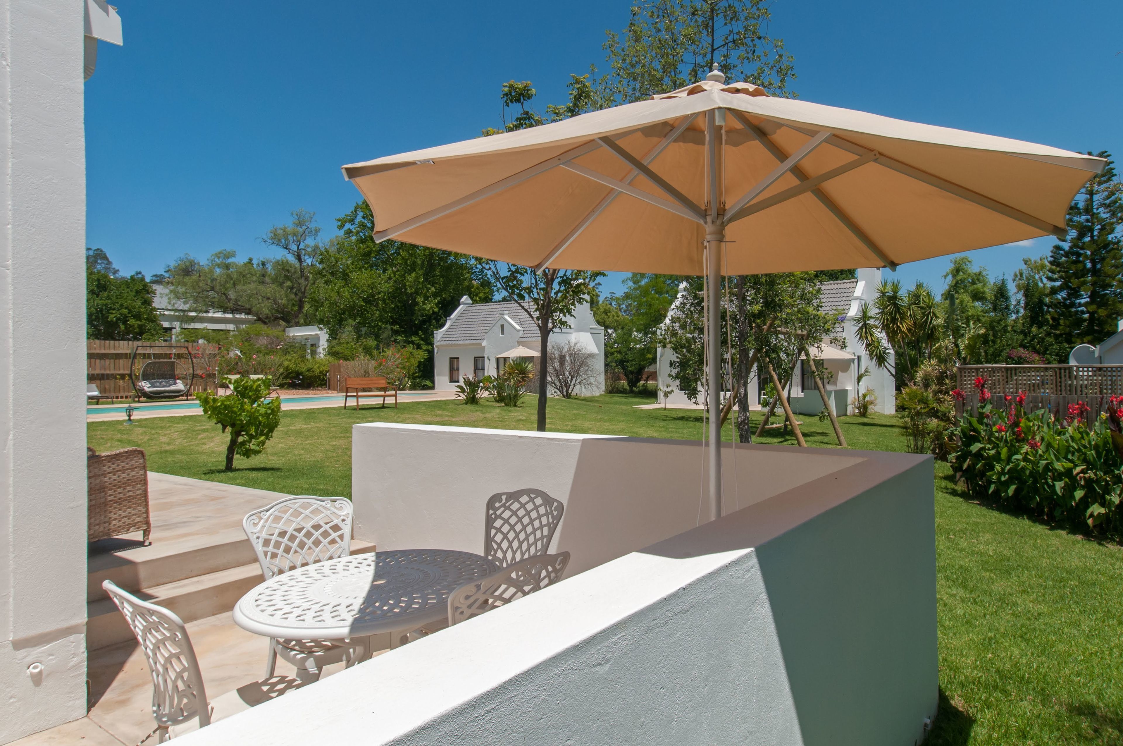 An outdoor patio with a table and chairs, a large umbrella, and a view of a residential neighborhood.