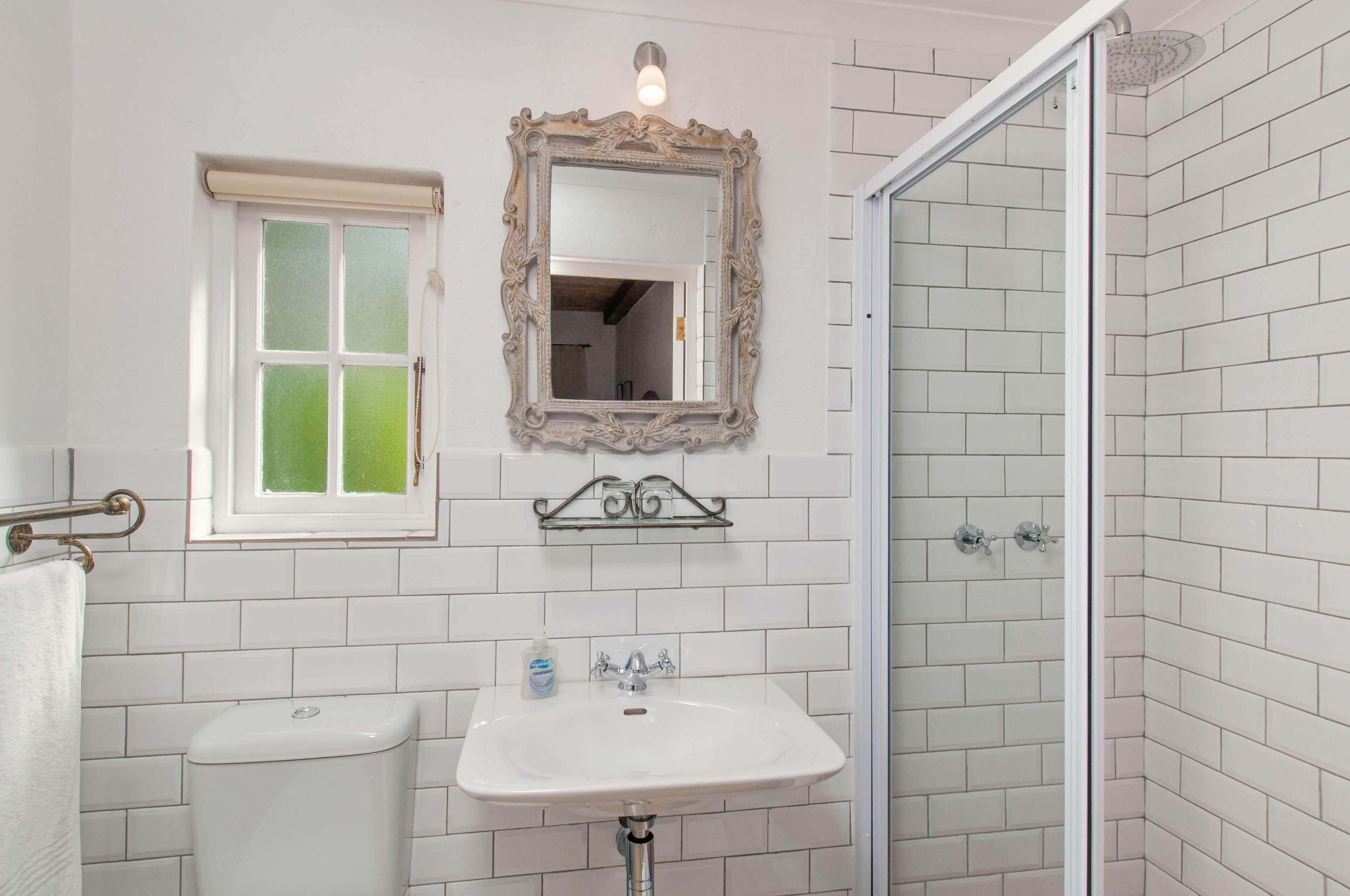 A bathroom with a white tiled wall, a sink, a toilet, a mirror, and a shower.