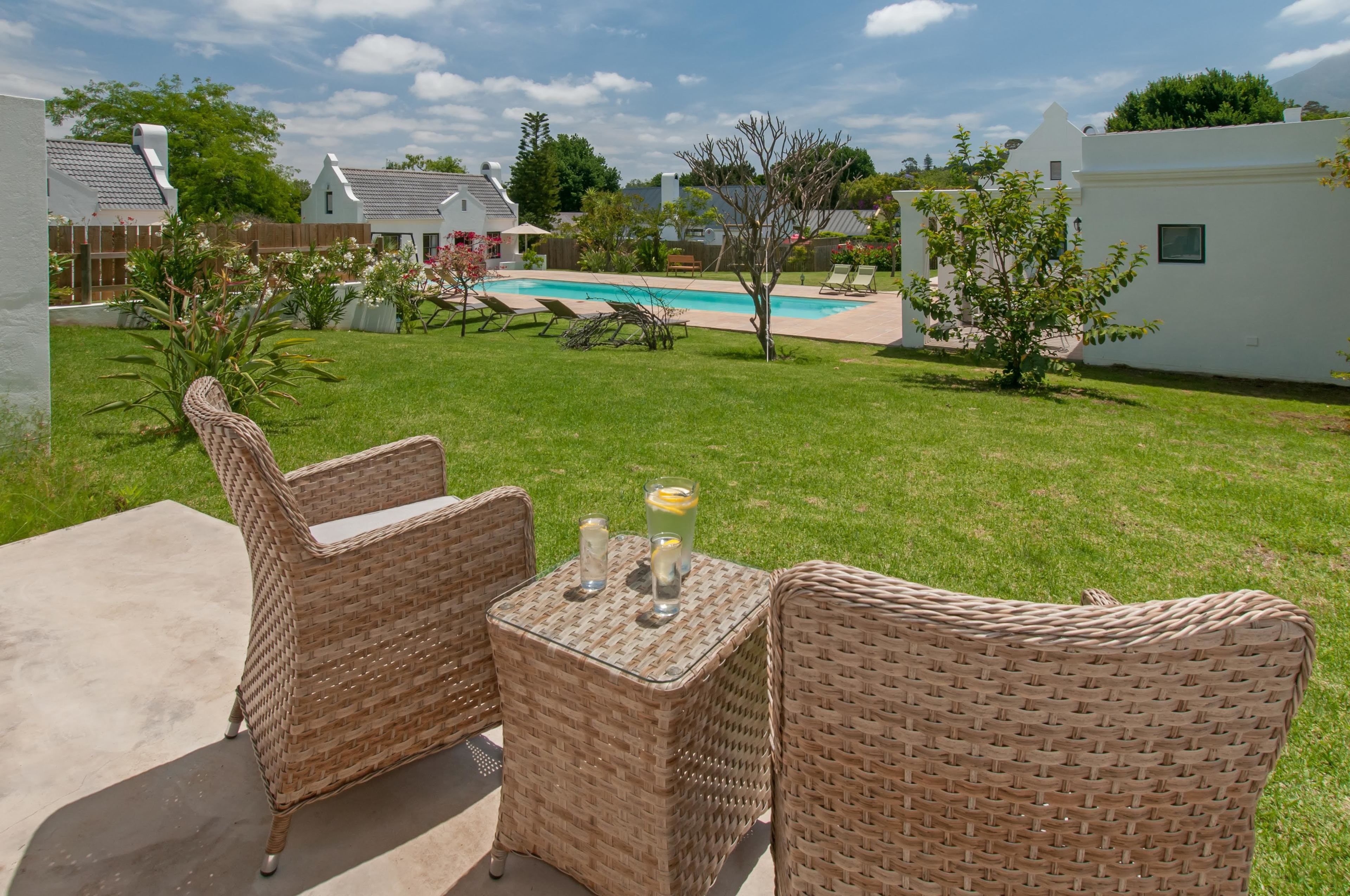 A backyard with a pool, wicker furniture, and a small table with drinks.
