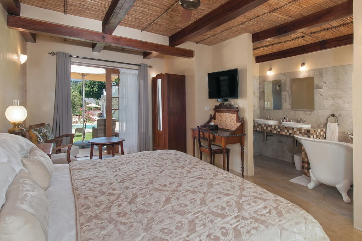 A bedroom with a large bed, a desk, a television, and a bathroom with a bathtub and sink.