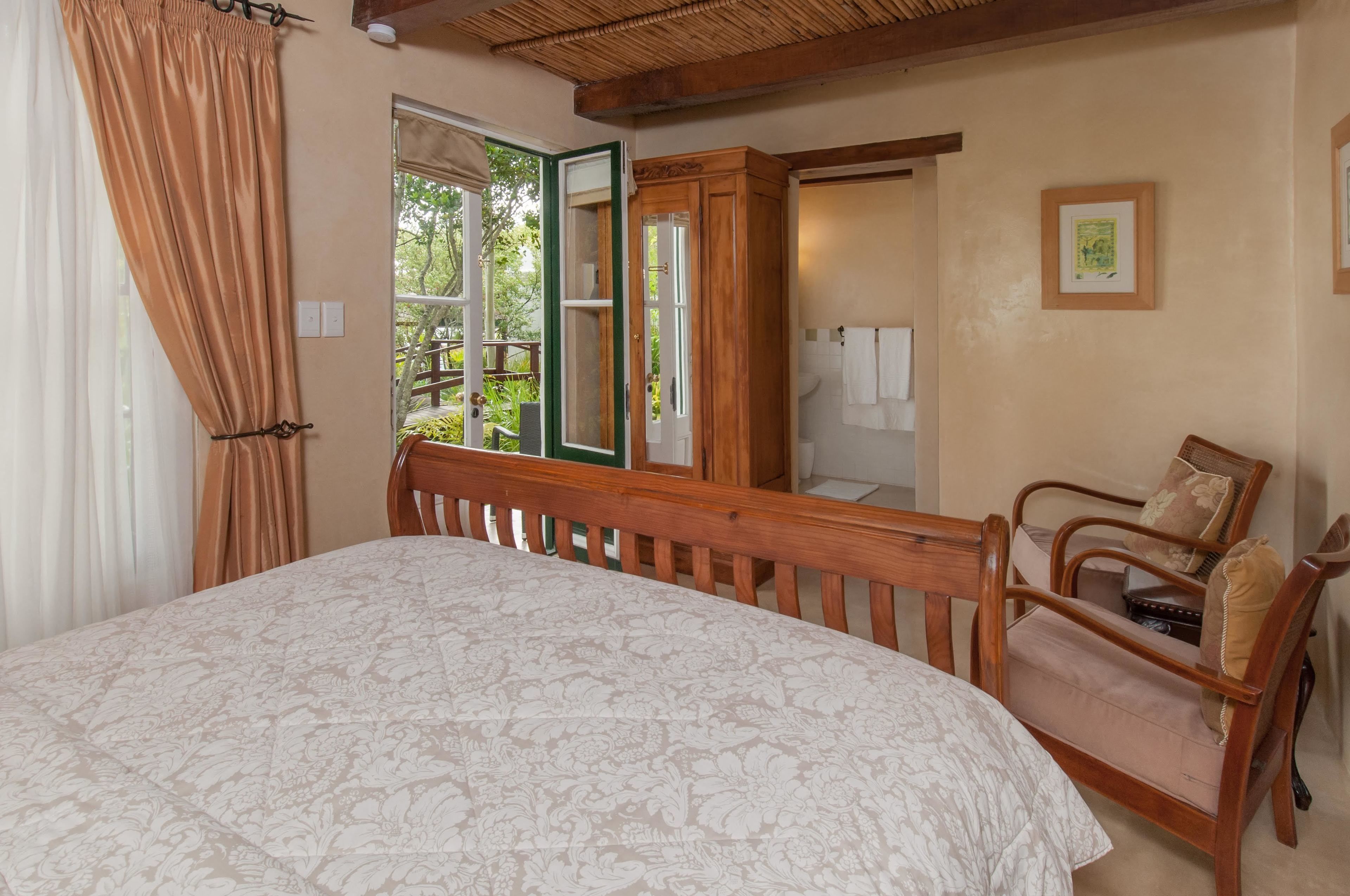 Un dormitorio con cama, cabecera de madera, una silla, armario y ventana con cortinas.