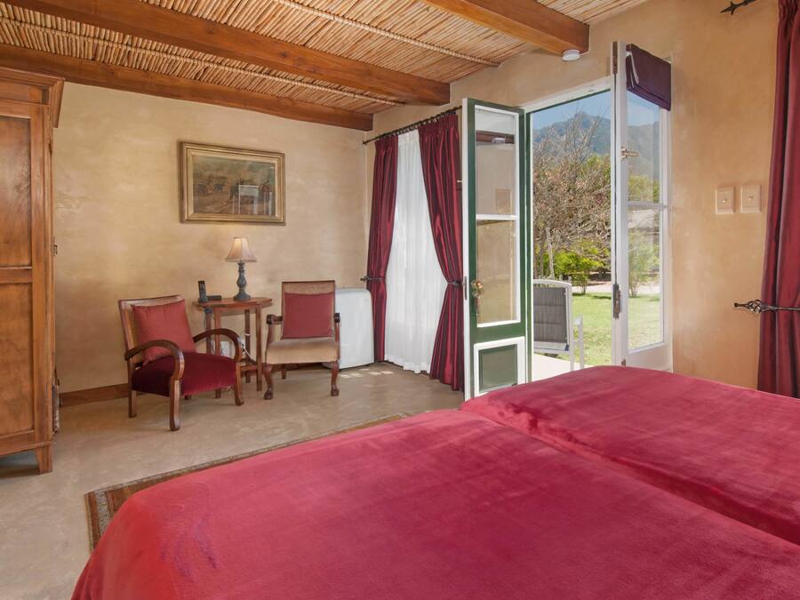 A room with a bed, two chairs, a table, and a painting on the wall.