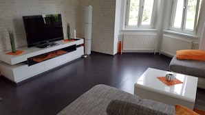 Un salon moderne avec un téléviseur à écran plat posé sur une console blanche, des canapés gris et une table basse blanche.