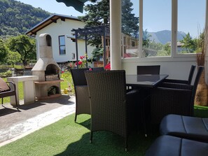 Eine Terrasse im Freien mit Korbmöbeln, einem Steinofen und Blick auf einen Berg.