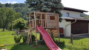 Une structure de jeu en bois avec un toboggan rouge, installée dans un espace herbeux.
