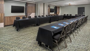 A conference room with a long table, chairs, a flat-screen TV, and a patterned carpet. - Troubadour Hotel (New Orleans)