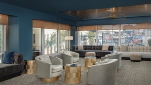 A modern lounge area with a patterned carpet, grey sofas, and round gold side tables. - Troubadour Hotel (New Orleans)