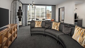 A modern living room with a curved sectional sofa, a wooden TV stand, and a patterned carpet. - Troubadour Hotel (New Orleans)