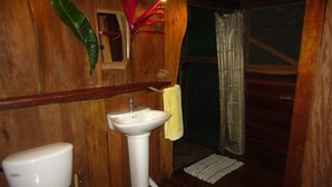 A wooden bathroom with a white sink, toilet, and a shower area. - EcoFarm Casa Pequeña (Drake Bay)