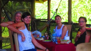 A group of people seated at an outdoor table with a red tablecloth, surrounded by greenery. - EcoFarm Casa Pequeña (Drake Bay)