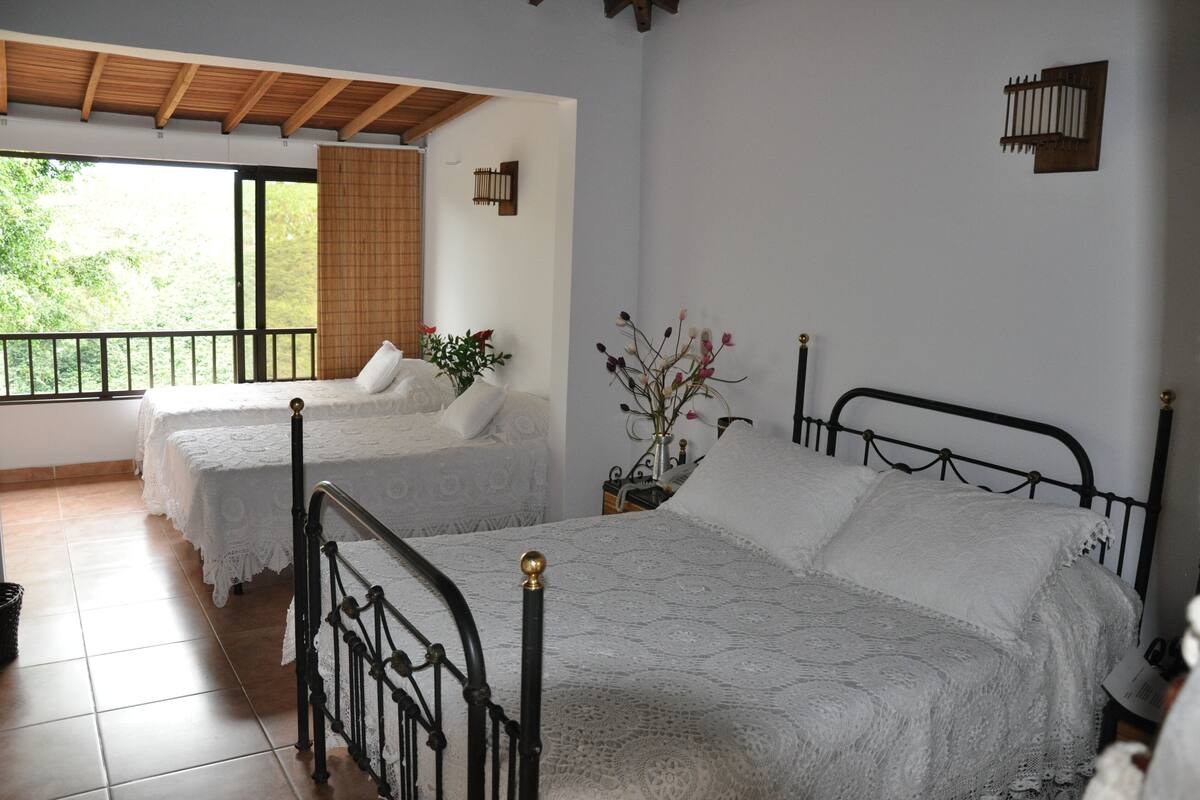 A bedroom with two beds, a balcony, and a view of greenery.