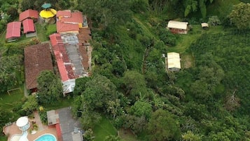 An aerial view of a residential area with multiple houses, a swimming pool, and dense surrounding vegetation.